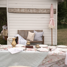 Load image into Gallery viewer, Outdoor setting with a table, bench, and 'The Chic Shed' sign.